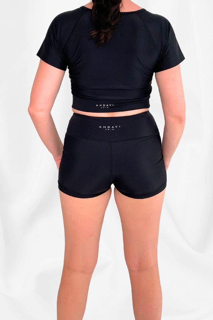 women with back turned wearing andavi swim short sleeve crop top and swim shorts in black