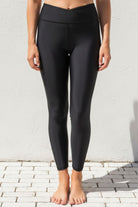 Person wearing black three quarter swim leggings standing against a light gray wall.