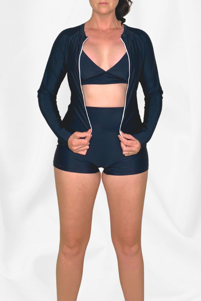 model wearing black front zip rash guard and black swim shorts with black triangle bikini top