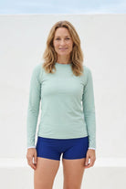 women wearing green rash guard and blue swim shorts against white wall