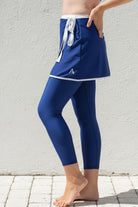 Person wearing a blue athletic swim skirt and leggings with a white logo against a light gray background