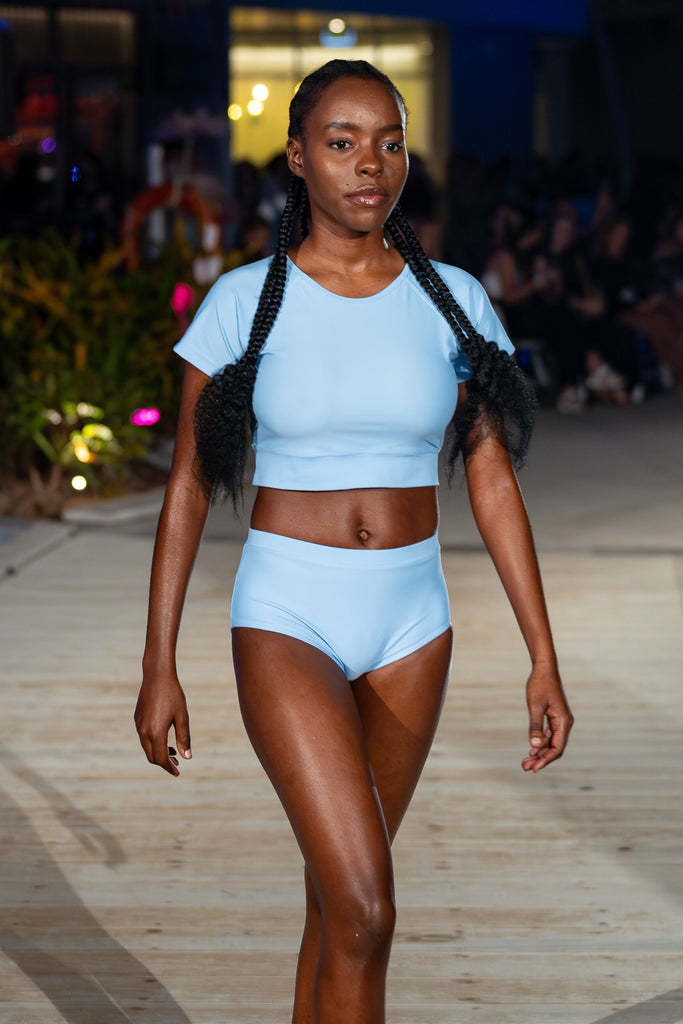 women on catwalk wearing light blue crop top rash guard and light blue bikini bottoms