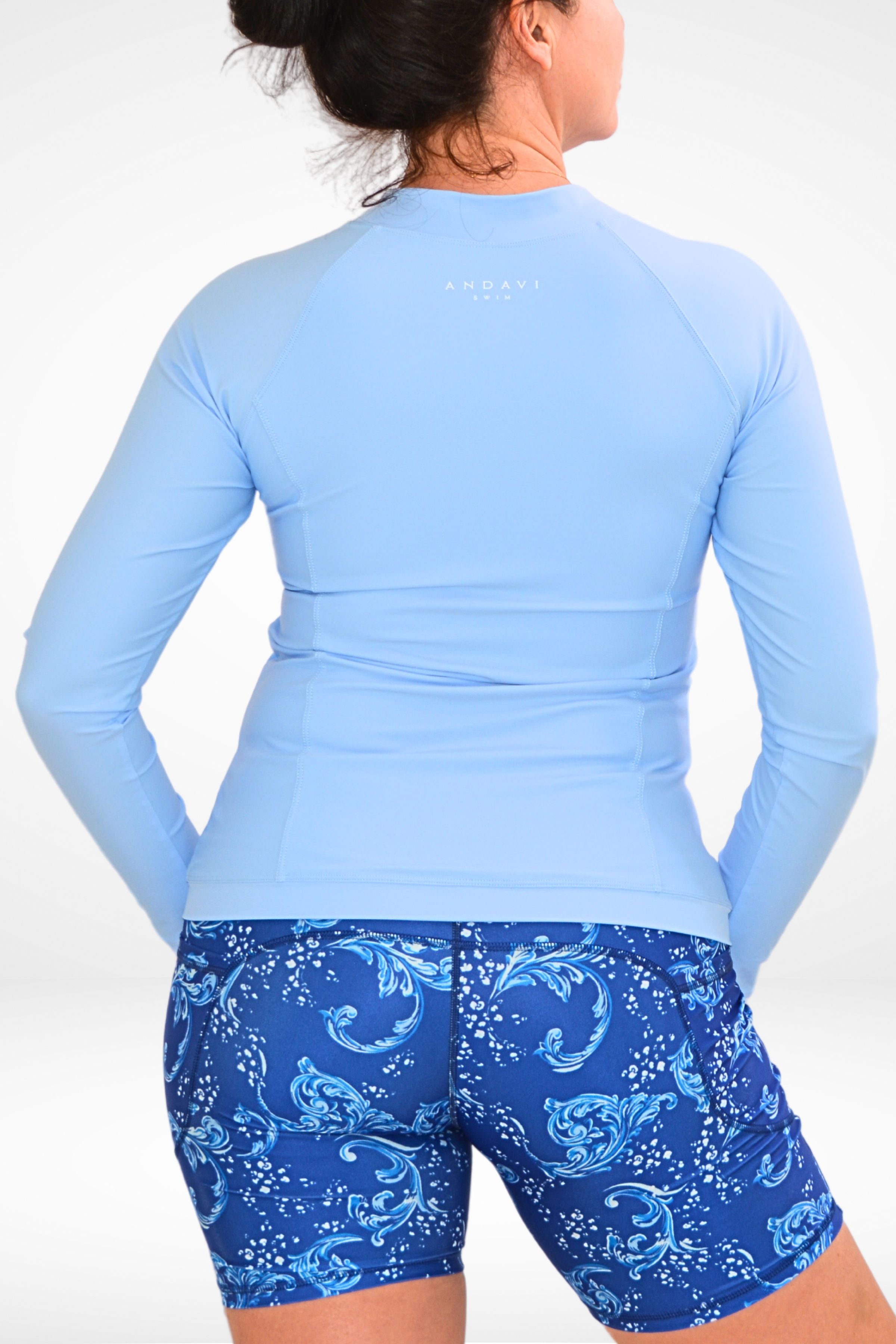 back view of a women wearong Andavi Swim long sleeve light blue rash guard and white and blue long leg swim active bike shorts