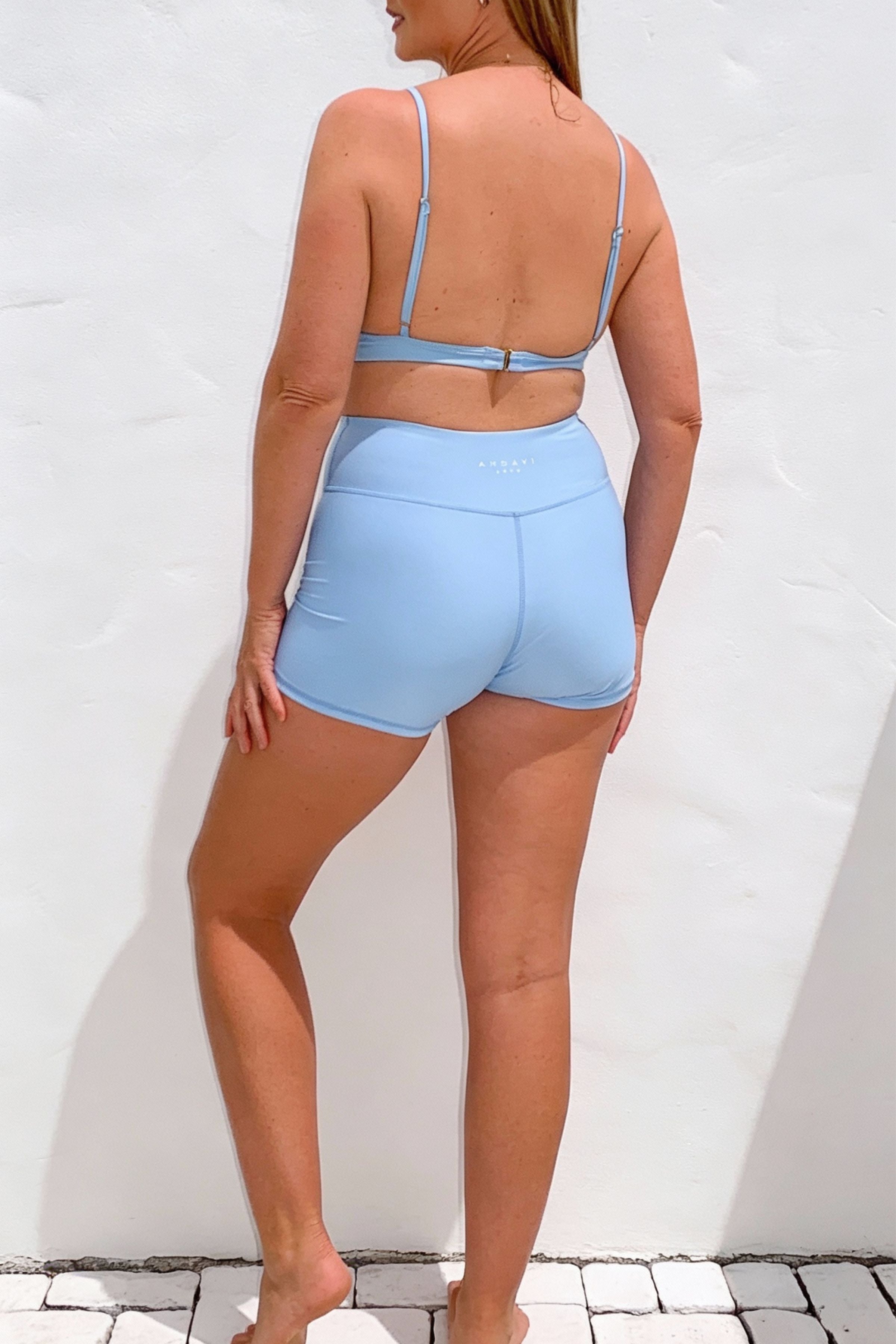 Woman wearing a light blue sports bra and shorts set against a white background