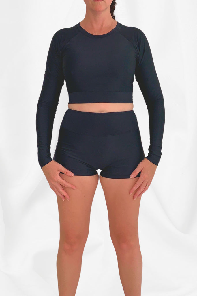model wearing long sleeve crop black swim top and black swim shorts