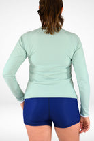 Person wearing a light green long-sleeve top and blue shorts on a white background
