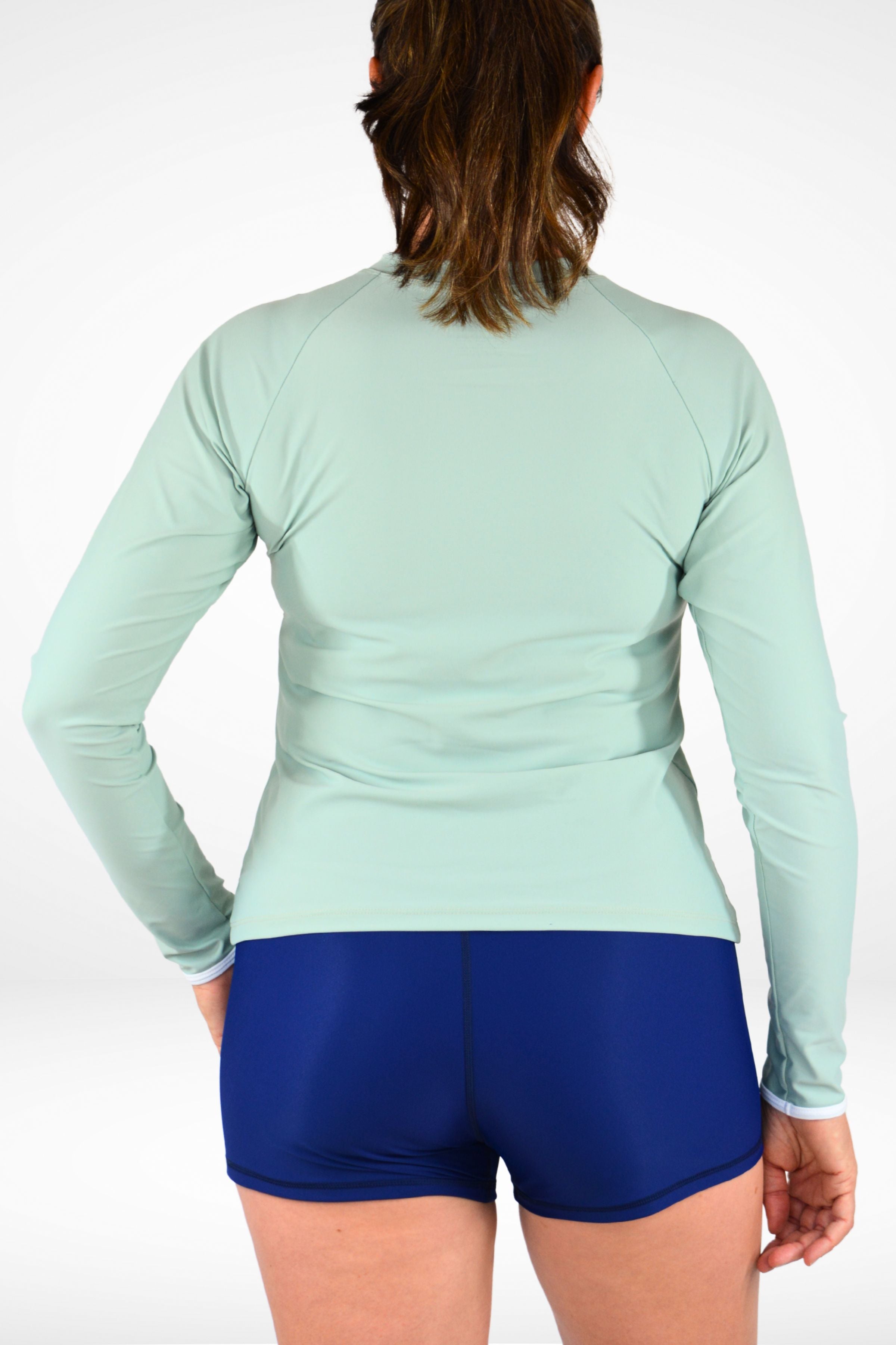 Person wearing a light green long-sleeve top and blue shorts on a white background