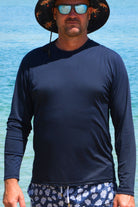 man wearing andavi long sleeve navy blue rash guard sunglasses and wide brim hat at the beach