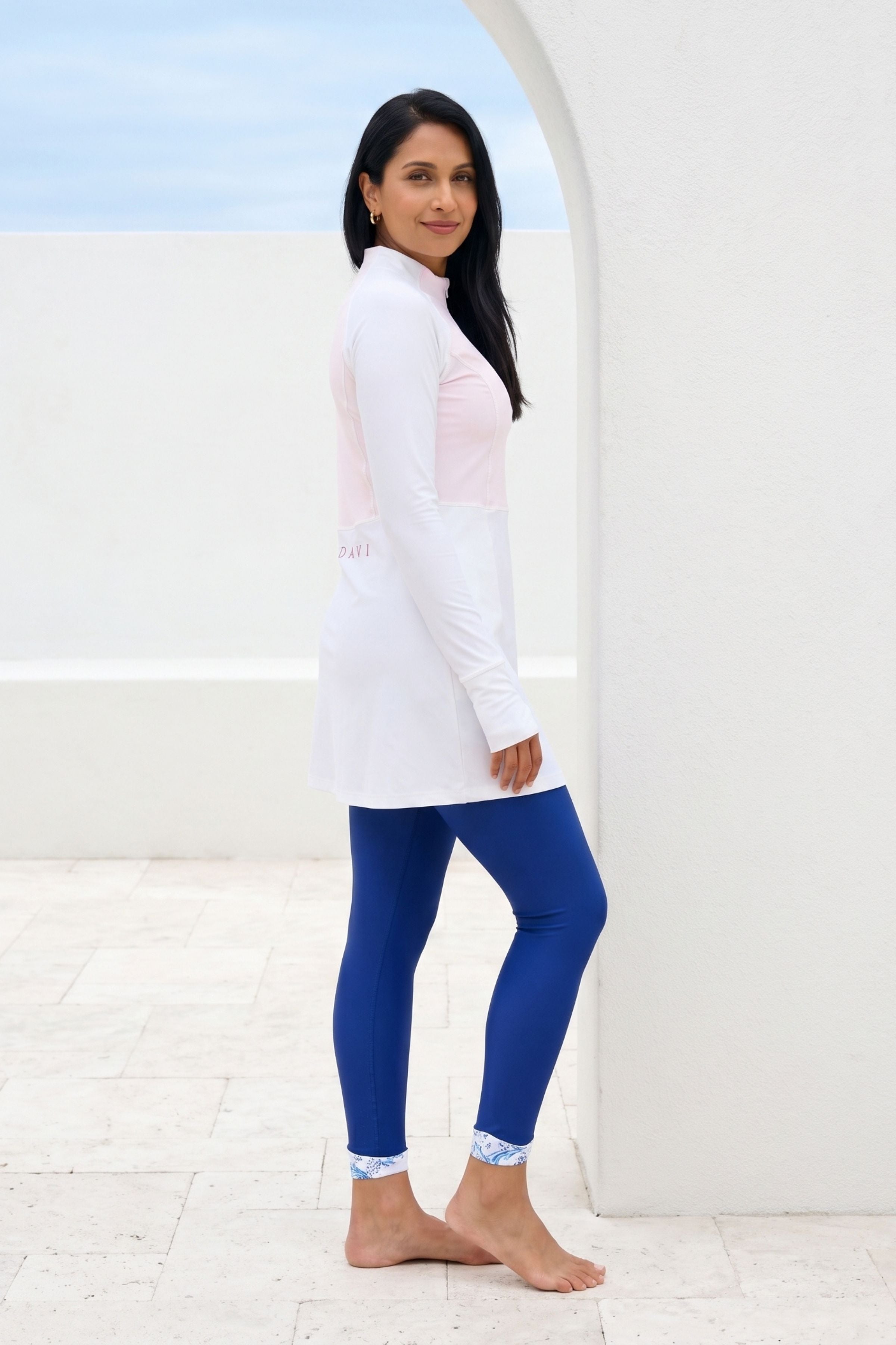 Woman wearing a white top and blue leggings standing against a white background