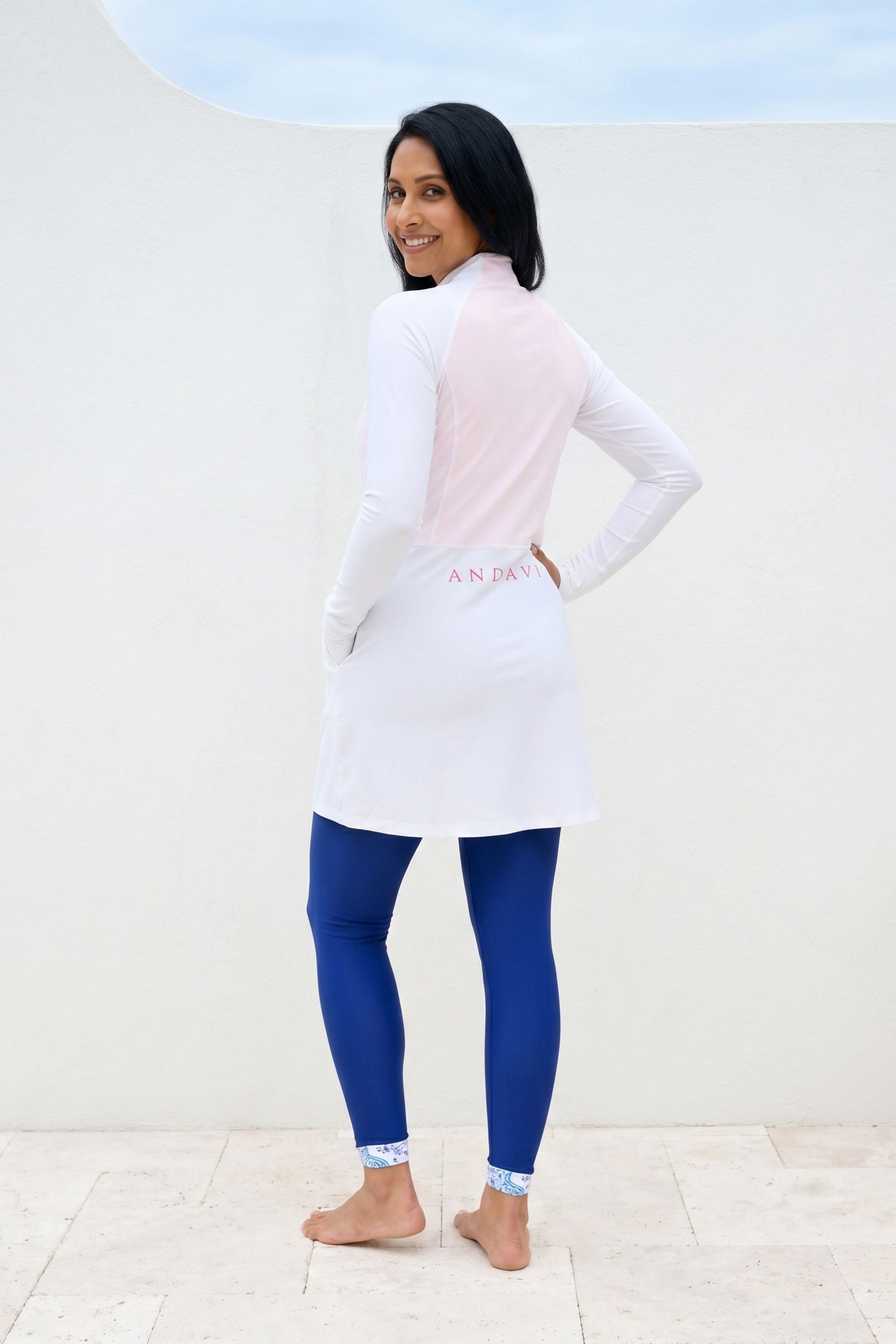 Woman wearing a white and pink long-sleeve top with blue leggings against a white background