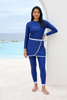 Woman wearing a blue swimsuit with white trim standing on a beach.