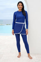 Woman wearing a blue swimsuit with white trim standing by a pool.