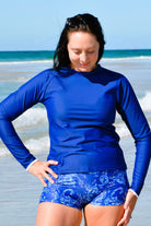 women on beach wearing navy blue rash guard and blue and white print swim shorts