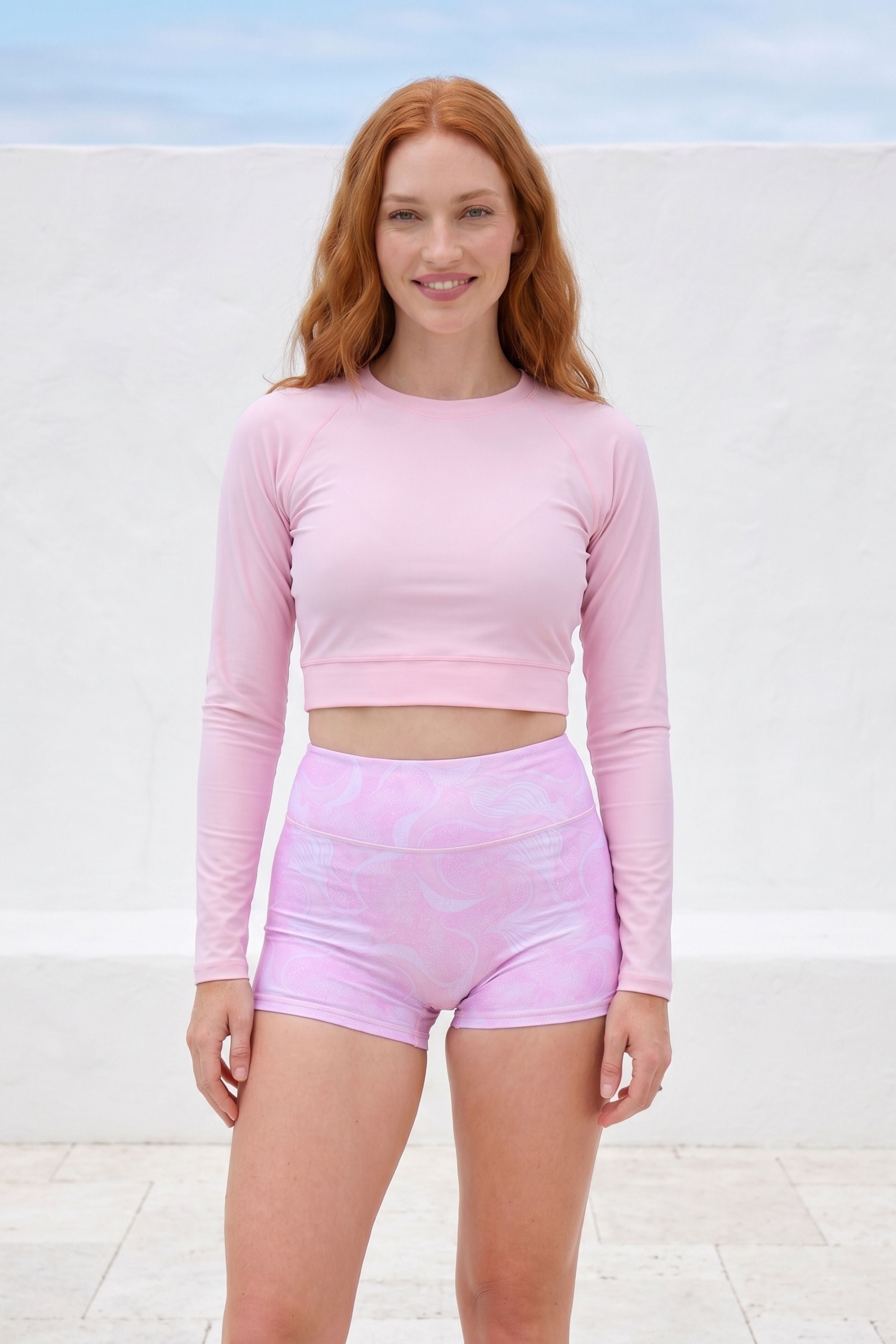 Woman wearing a pink long-sleeve top and shorts against a white background