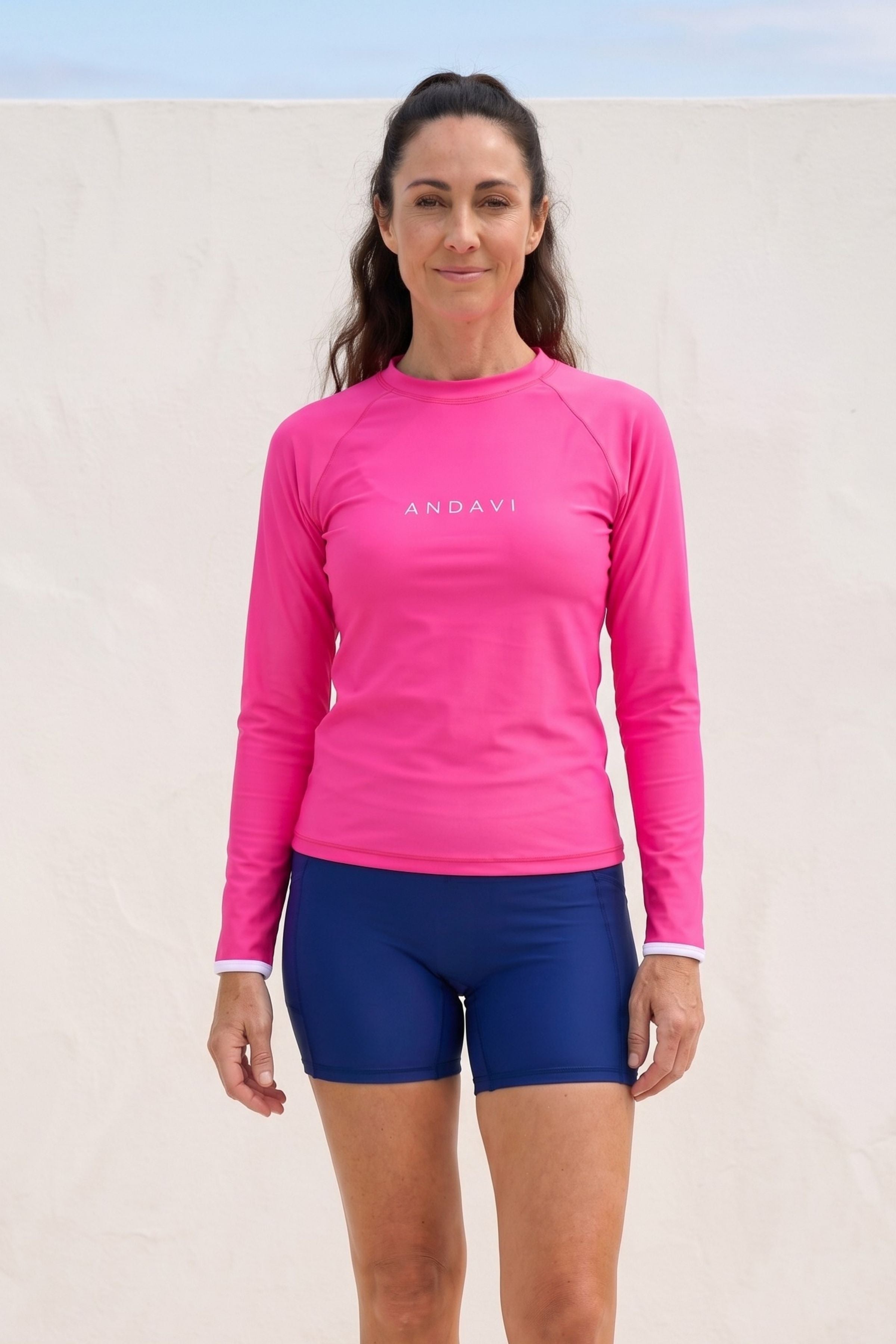 Woman wearing a pink long-sleeve shirt and blue shorts with 'ANDAVI' branding on a light background