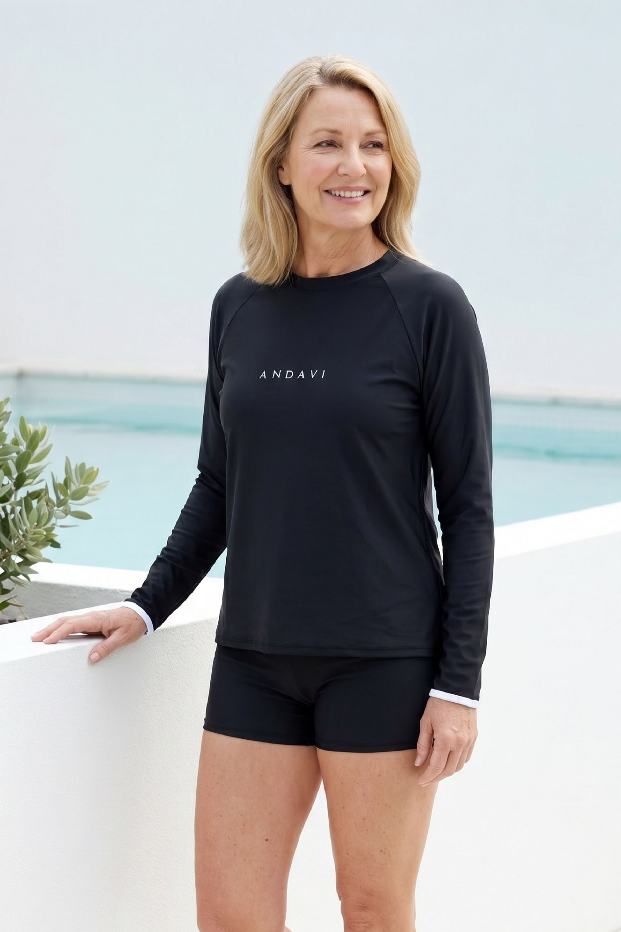 women standing in front of a pool and white wall wearing andavi black rash gaurd and andavi black swim shorts