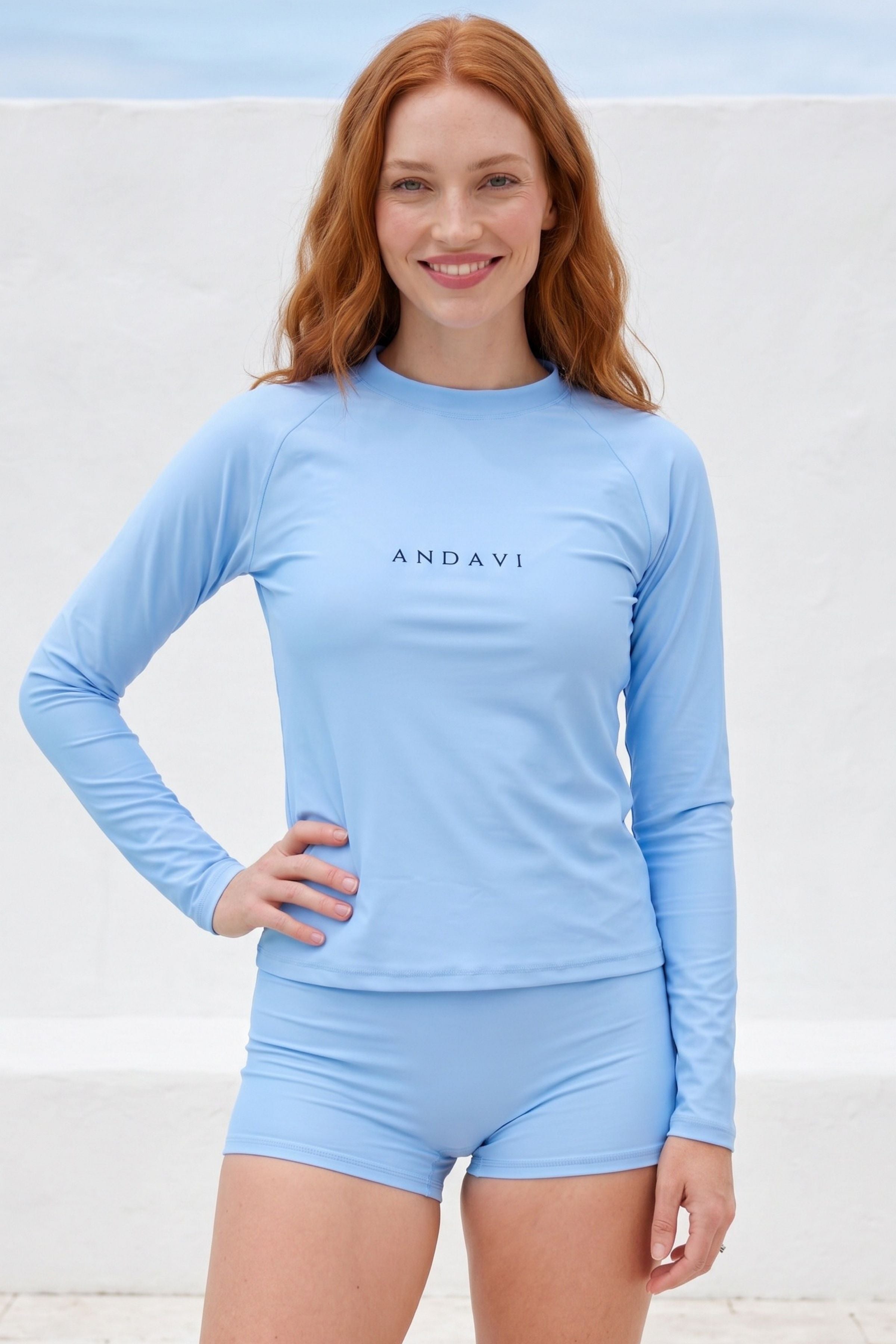 women wearing light blue andavi rash guard and swim shorts in front of white textured wall 