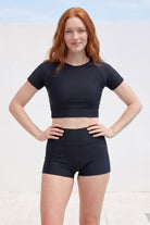 Person wearing a black crop top and shorts on a light background