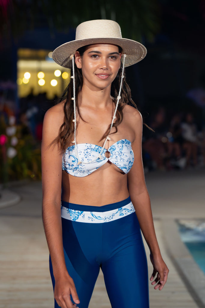 model on catwalk wearing straw hat white and blue bandeau bikini top and white and blue leggings