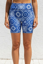 Blue patterned shorts worn by a person against a white textured wall.