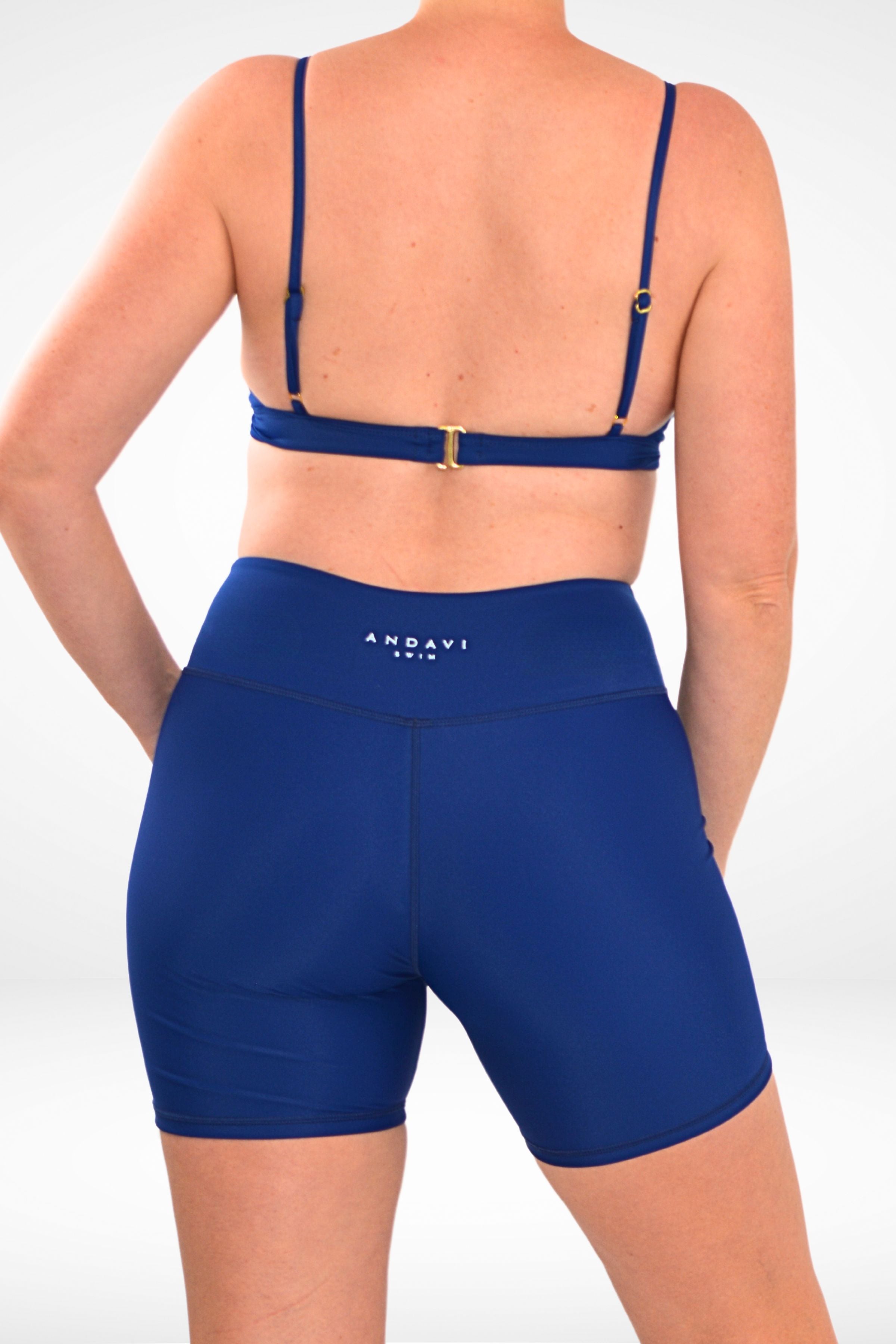 back view of a model wearing Andavi Swim long leg swim active bike shorts and matching bikini top in dark blue