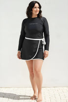 Woman wearing a black long-sleeve top and skirt with a white border against a light background