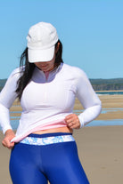 women looking downward wearing white long sleeve rash guard and white and blue swim leggings