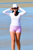 model on the beach wearing white long sleeve rash guard and white and pink swim shorts 