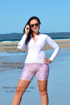 model on the beach wearing white long sleeve rash guard and floral swim bike shorts