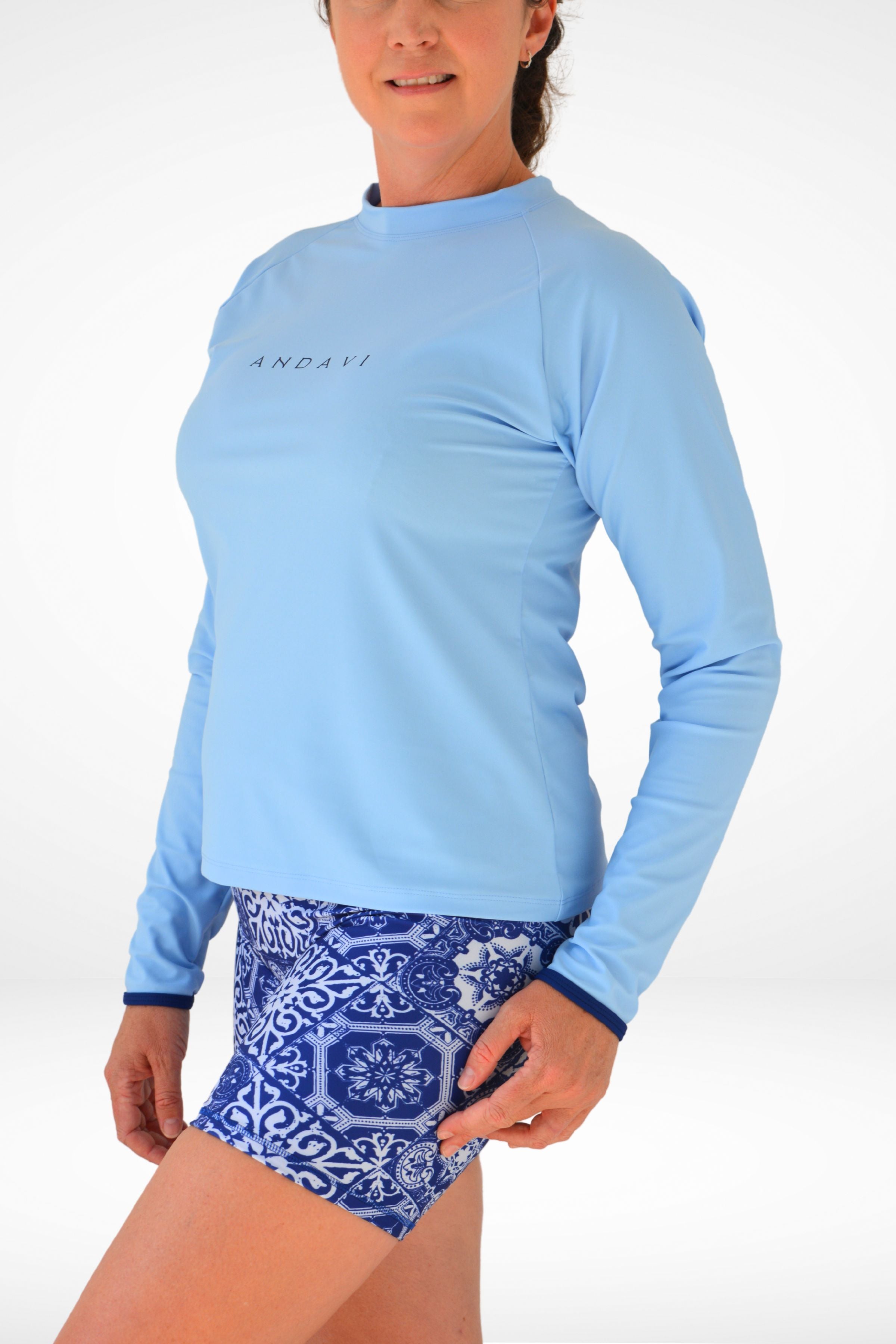 Person wearing a light blue long-sleeve shirt and blue patterned shorts on a white background