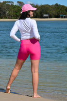 Person wearing a white long-sleeve shirt and pink shorts standing on a beach.