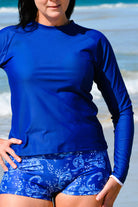 women on beach wearing blue white print swim mshorts and dark blue long sleeve rash guard