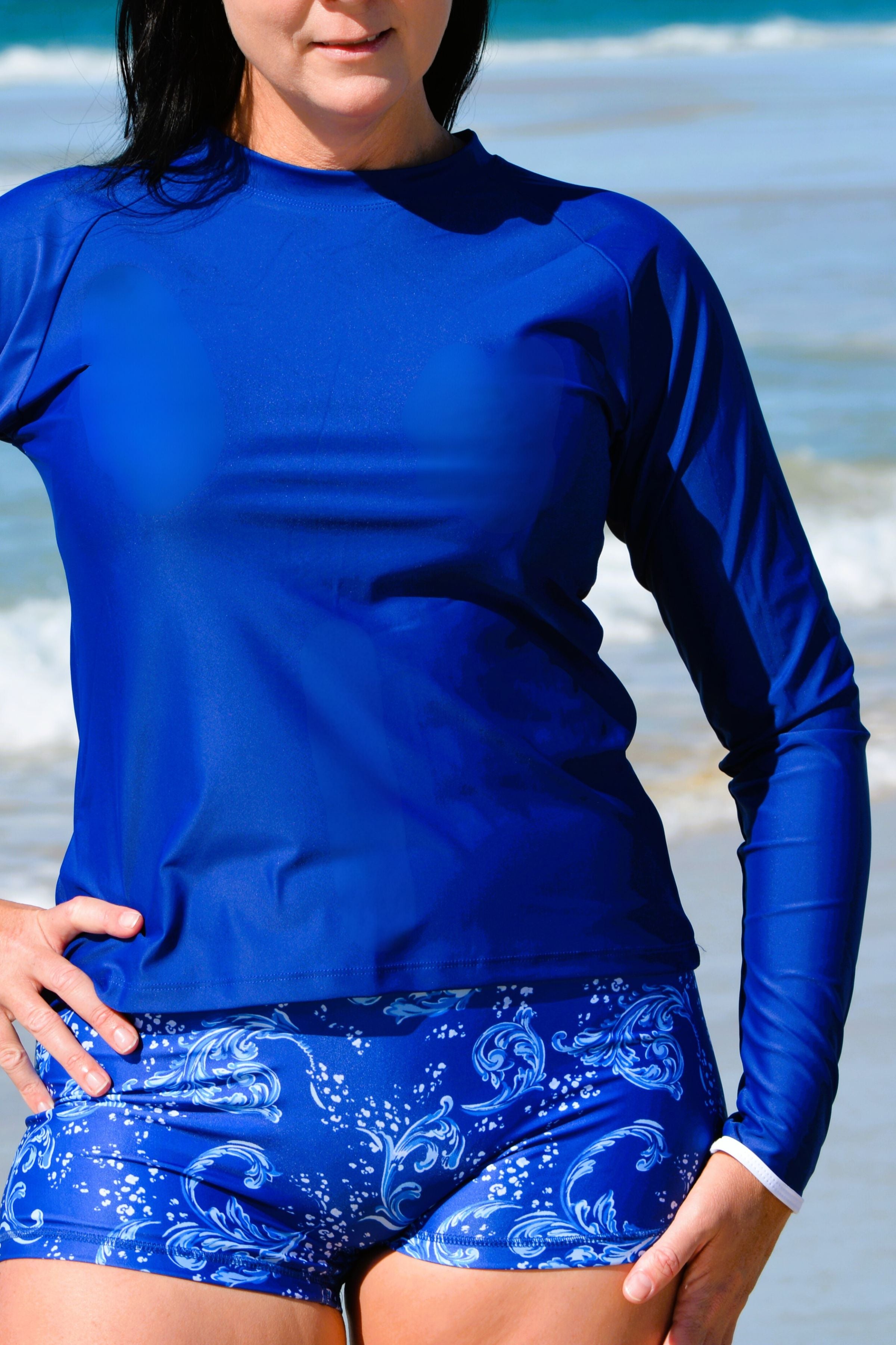 women on beach wearing blue white print swim mshorts and dark blue long sleeve rash guard