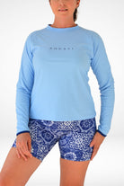 Woman wearing a blue long-sleeve shirt and patterned shorts on a white background