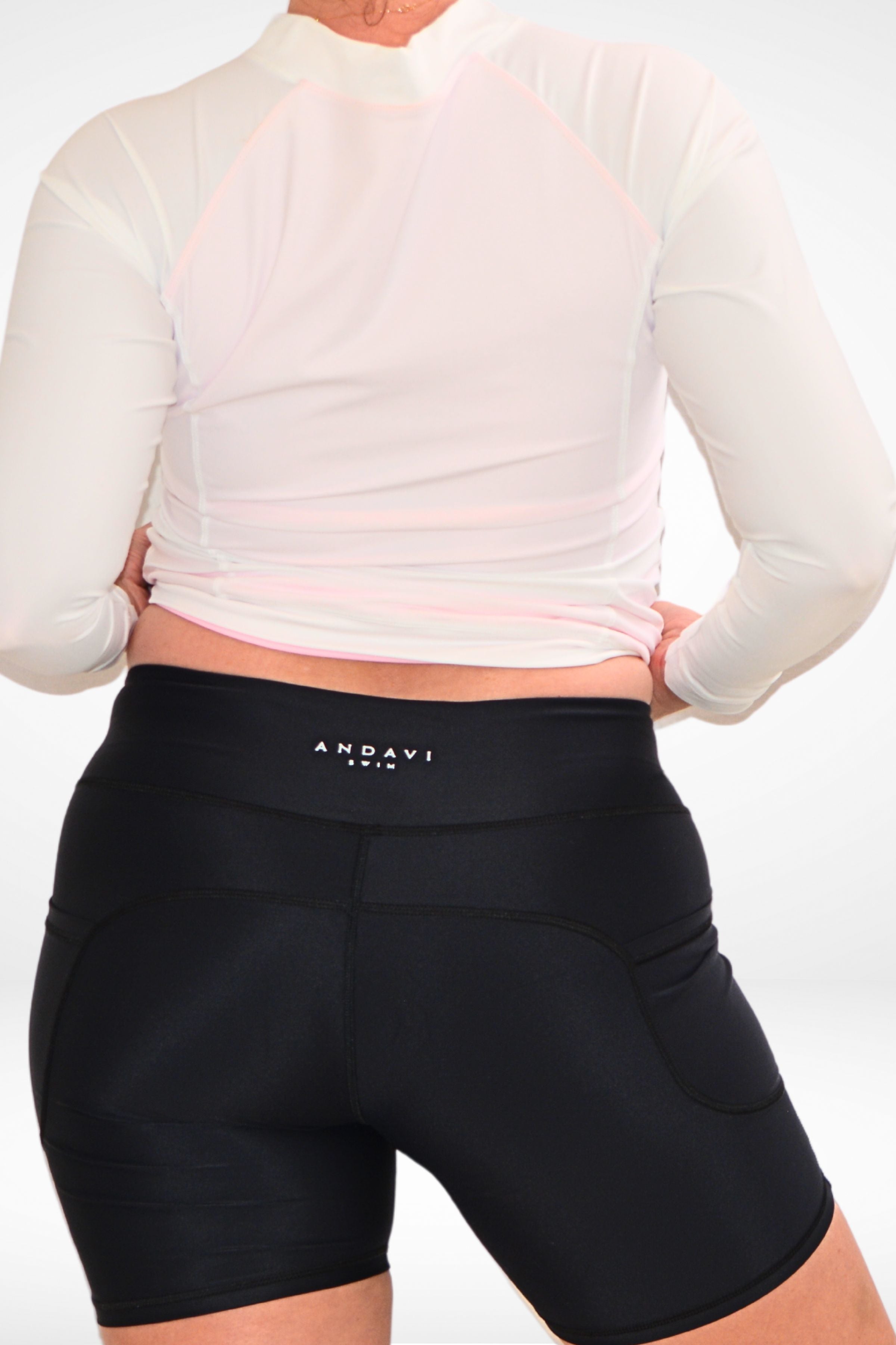 back view of model wearing andavi swim black swim active pocket bike shorts and long sleeve white rash guard