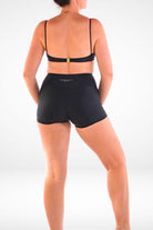 back view of a women wearing black bikini top with gold back clasp and Andavi Swim logo black swim shorties