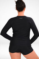 back view of a women wearing andavi swim long sleeve black rash guard and black swim shorts