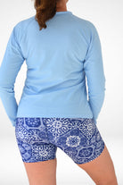 Person wearing a light blue long-sleeve top and blue patterned shorts on a white background