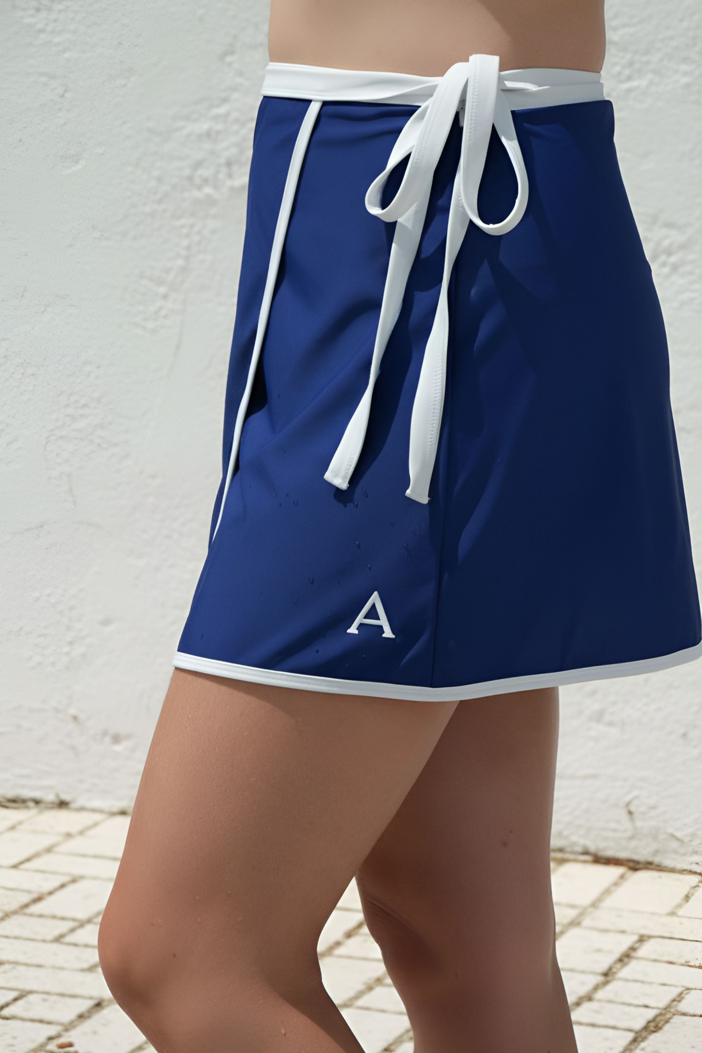 Blue athletic wrap swim skirt with white drawstring and trim on a person against a white background